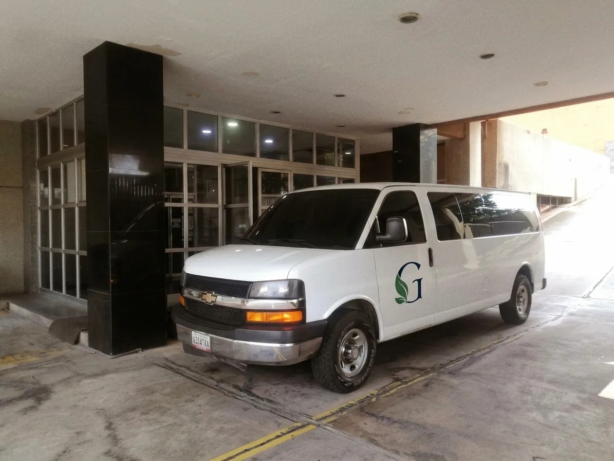 Camioneta de pasajeros blanca con el logo de Green Life frente a un edificio