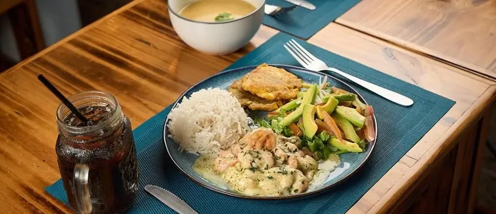 Plato con camarones, arroz, tostones y ensalada de aguacate sobre mesa de madera